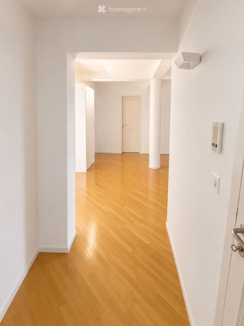 Empty hallway with light wooden flooring, white walls, and a single door at the end.
