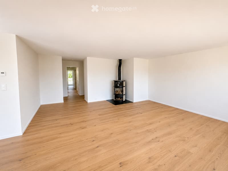 Empty room with light wooden flooring, white walls, and a fireplace in the center.