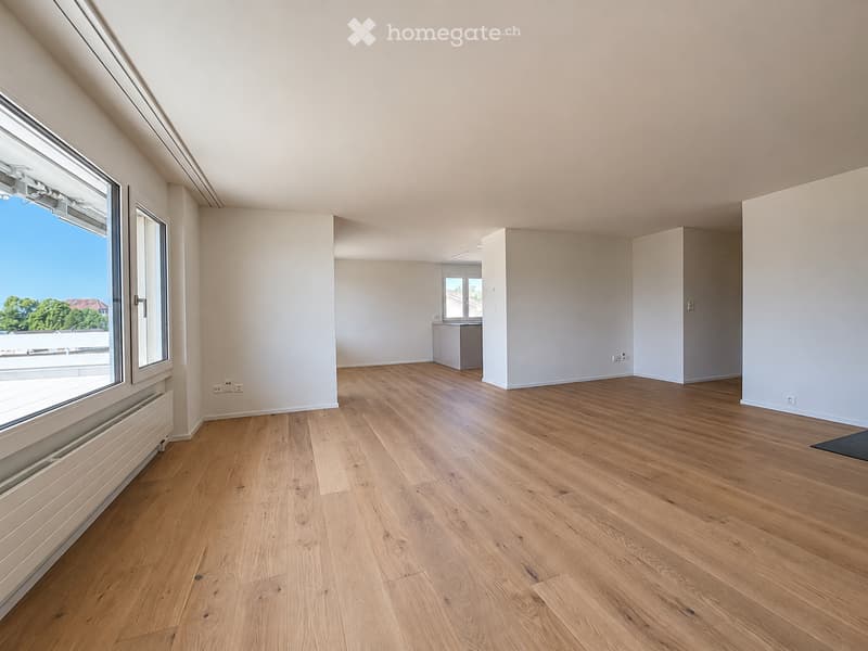 Empty room with wooden flooring, white walls, large windows, and a small cabinet in the background.