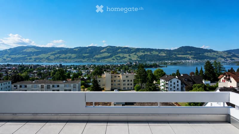 Balcony overlooking a scenic lake and distant mountains, with a white railing and tiled floor.