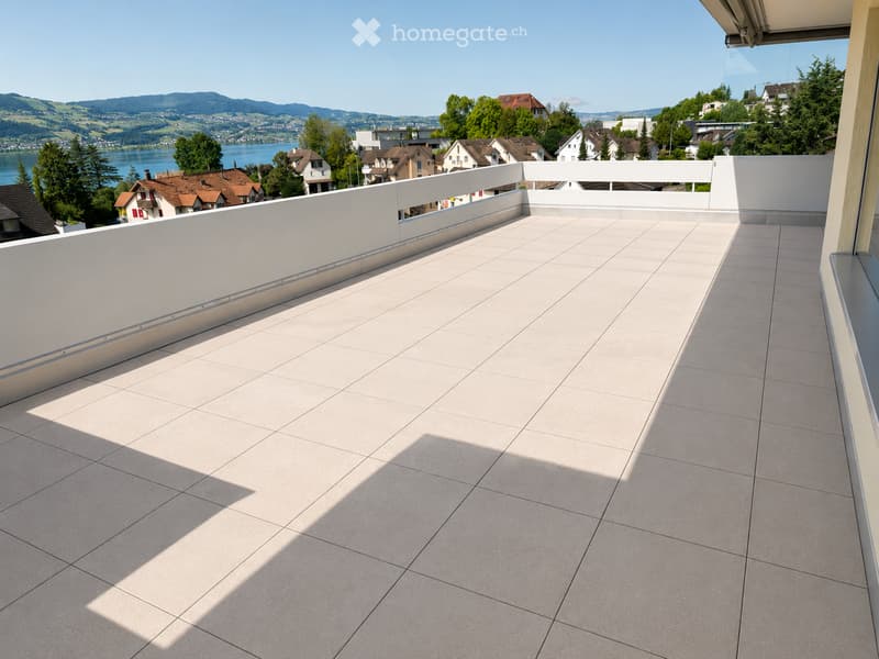 Modern balcony with tiled flooring, white railing, and scenic view of a lake and surrounding landscape.