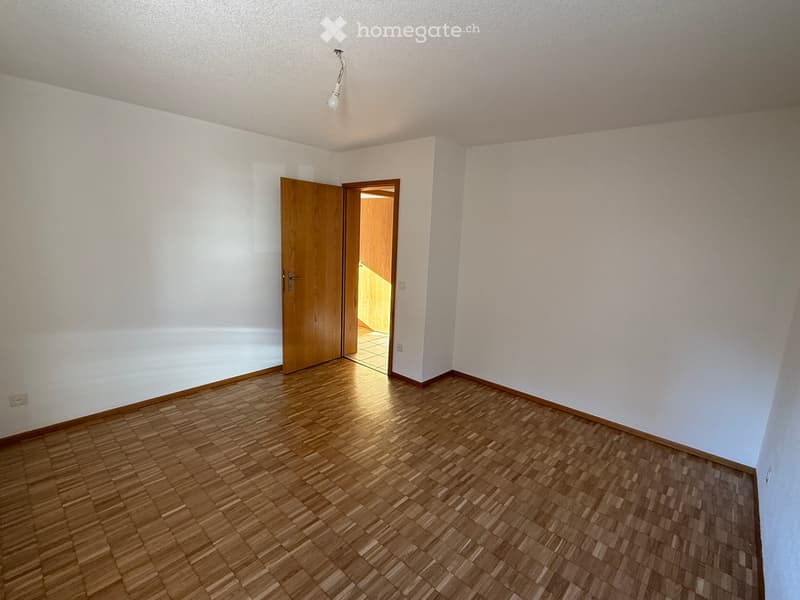 Empty room with wooden flooring, white walls, and a single wooden door leading to another room.