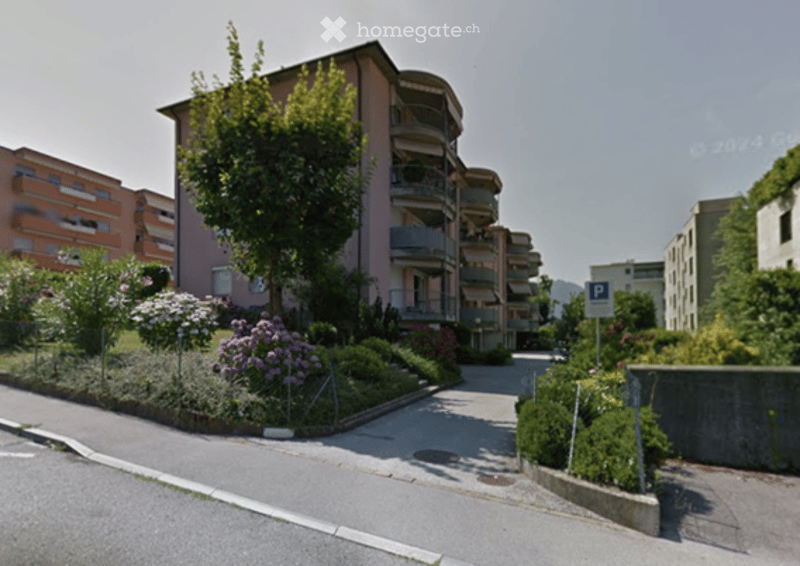 Multi-story residential building with balconies, surrounded by greenery and a well-maintained garden area.