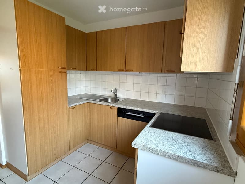Modern kitchen with light wooden cabinets, granite countertops, and stainless steel appliances including a sink, faucet, dishwasher, and electric stove.