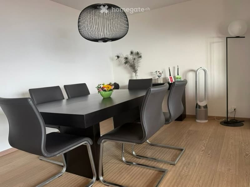 Modern dining room with a black dining table, six black chairs, a flower vase, a floor lamp, and an air purifier. The room features a large, spherical pendant light and a sleek design.