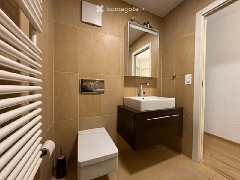 Modern bathroom with beige tiles, a white sink with a dark wooden cabinet, a toilet, a mirror, and a white radiator.