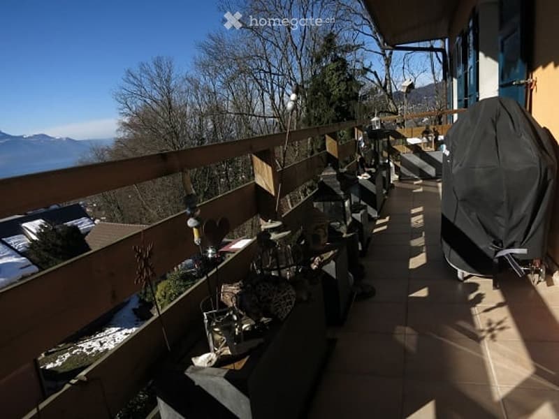 Balcony with wooden railing, tiled floor, scenic mountain view, and some outdoor furniture.