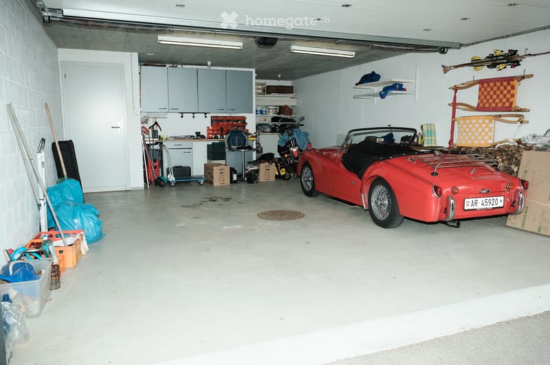 Garage with a red convertible car, shelves, tools, and storage items.