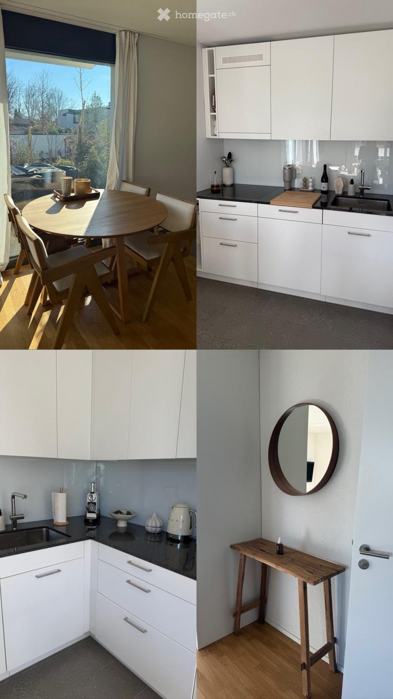Modern kitchen with white cabinets, stainless steel sink, coffee maker, and a small wooden table with chairs in a bright, sunlit area.