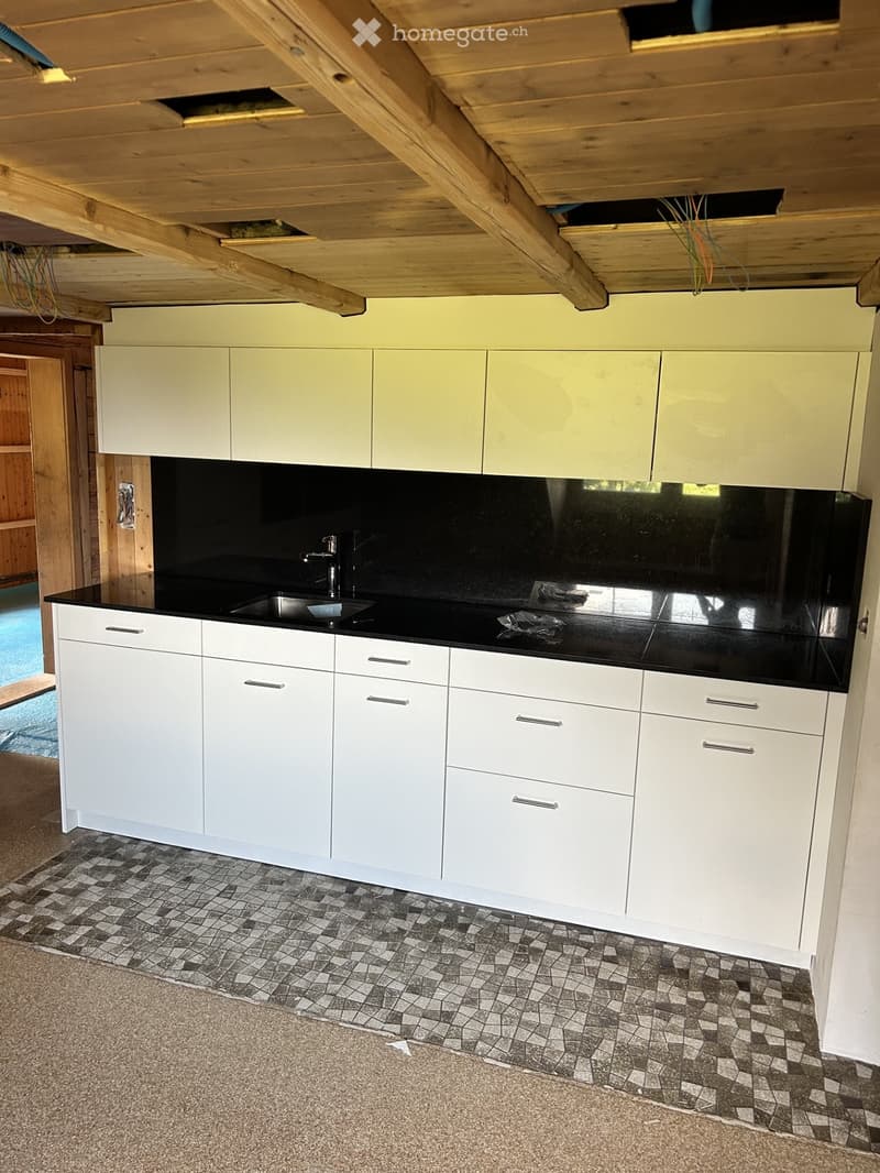 Modern kitchen with white cabinets, black countertop, and mosaic tile flooring. Features a sink with a chrome faucet and visible wooden beams on the ceiling.