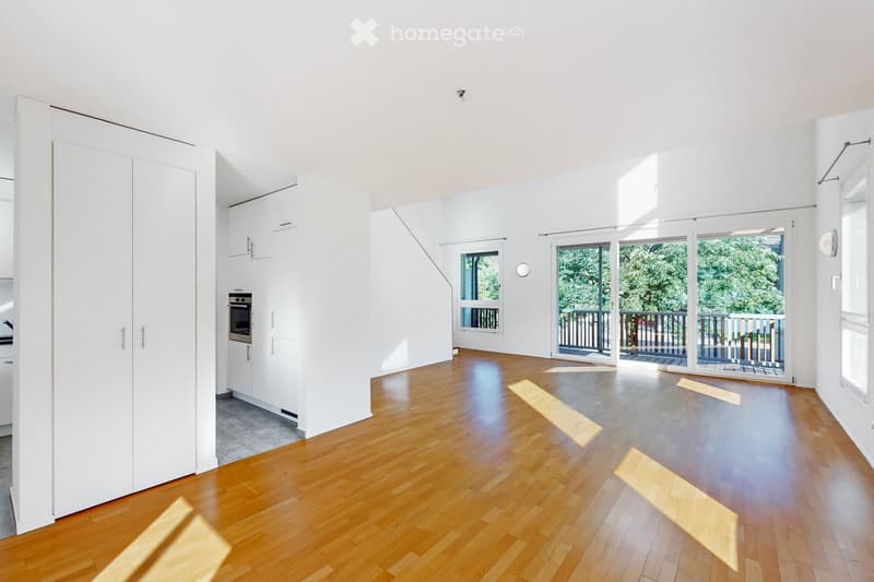 Bright, open room with wooden flooring, white walls, large sliding glass doors leading to a balcony, and built-in white cabinetry.
