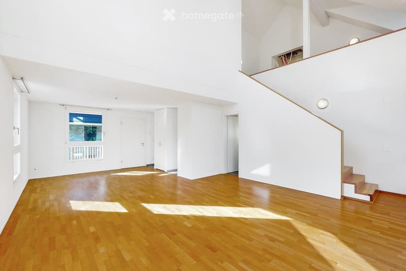 Bright, open-plan room with wooden flooring, white walls, large windows, and a staircase leading to an upper level.