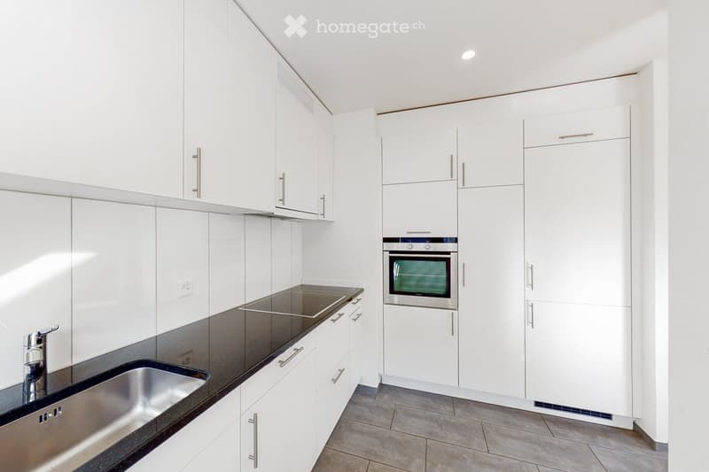 Modern kitchen with white cabinets, black countertops, stainless steel sink, and built-in oven.