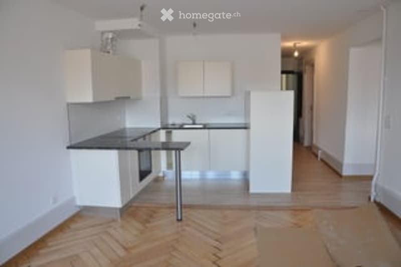 Modern kitchen with white cabinets, dark countertop, and a small dining table. Wooden herringbone flooring.