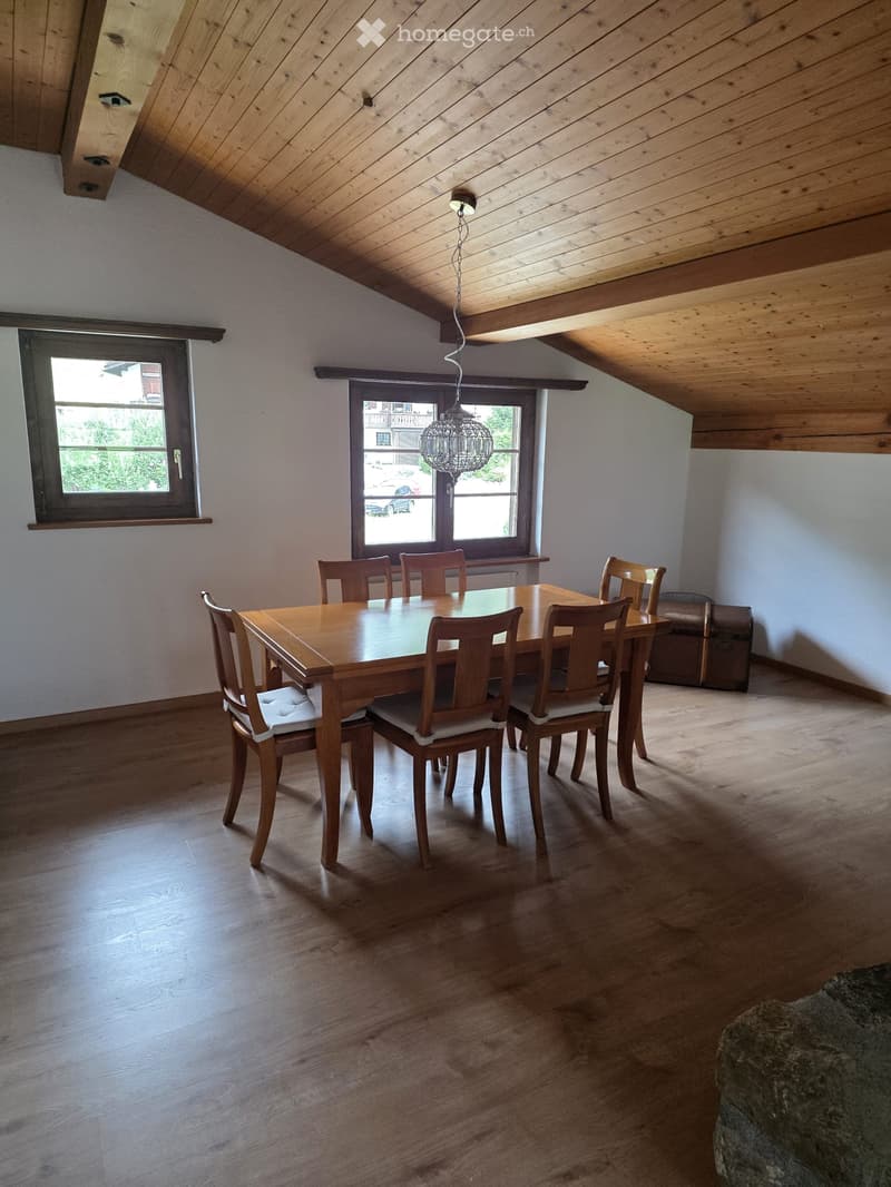 Dining room with wooden floor, slanted wooden ceiling, pendant light, dining table with six chairs, and a small bench near the window.