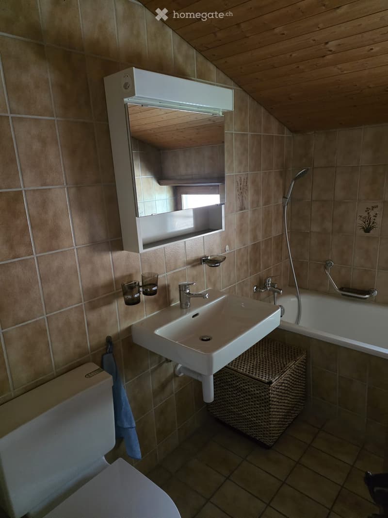 Bathroom with beige tiled walls and wooden ceiling, featuring a white sink, mirror, toilet, bathtub, and two cups on a shelf.