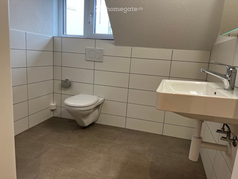 Modern bathroom with white tiled walls, a toilet, a sink with a chrome faucet, and a window above the sink.