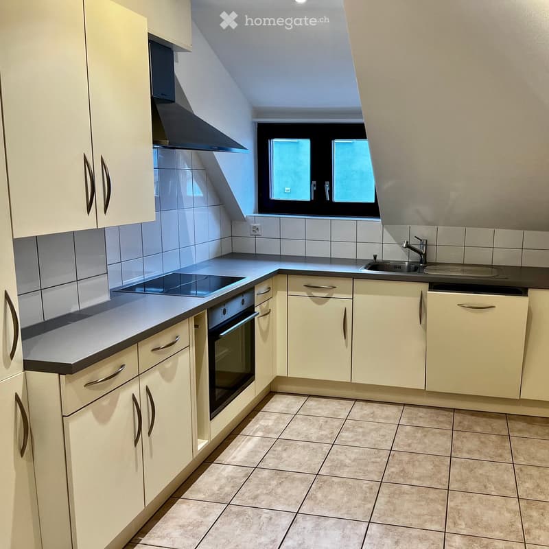 Modern kitchen with light-colored cabinets, stainless steel appliances, and a tiled floor. Features an oven, range hood, sink, and faucet.