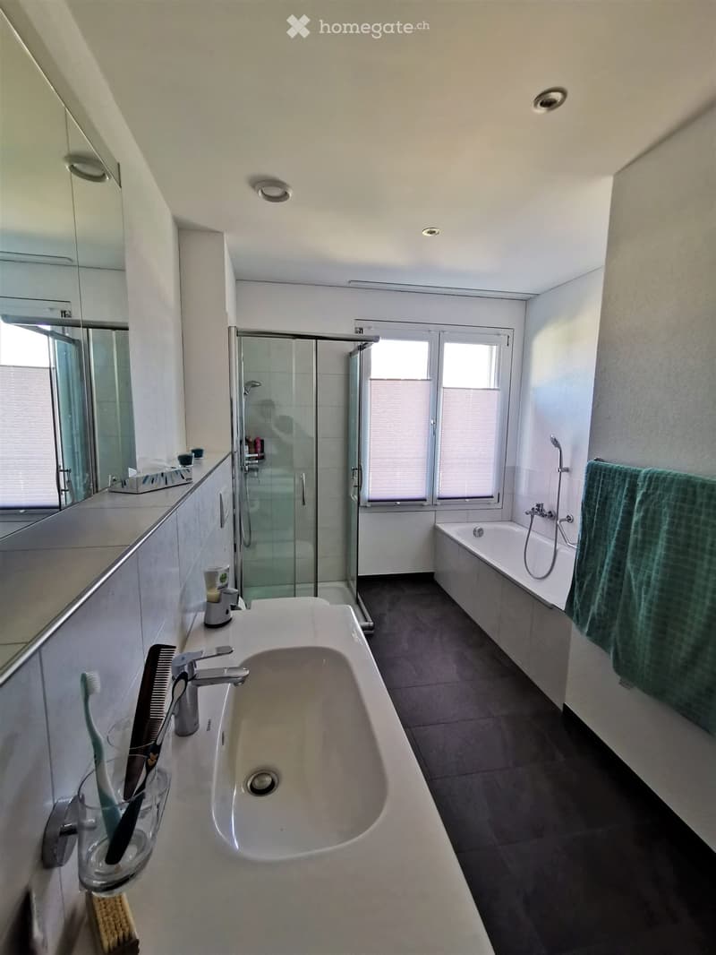 Modern bathroom with a large sink, bathtub, shower, and mirror. Includes a toothbrush, comb, and towel.