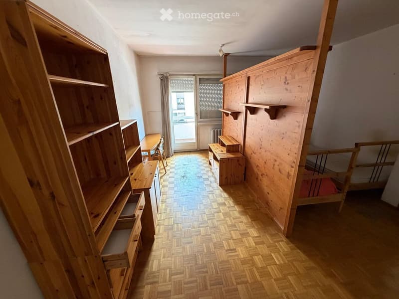 Empty hallway with wooden flooring, built-in wooden shelving units on both sides, and a small table and chair near the door.