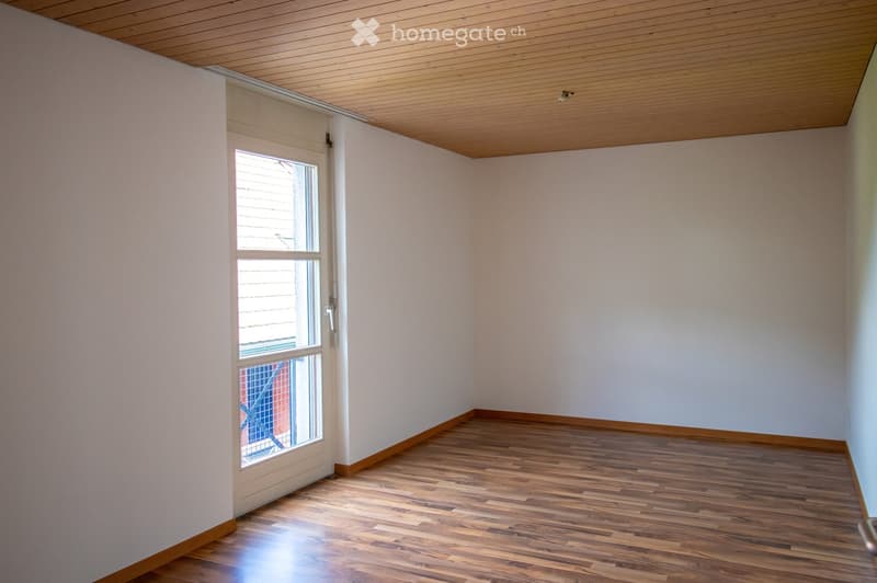 Empty room with wooden flooring, white walls, and a large window with blinds. The ceiling is finished with wood paneling.