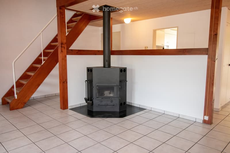 Hallway with tiled floor, wooden staircase, and a black wood-burning stove with a chimney pipe.