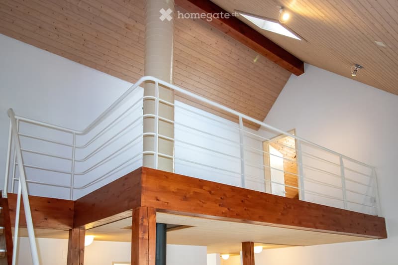 Open-concept interior with wooden ceiling, white walls, and a raised wooden platform accessed by a white metal staircase.