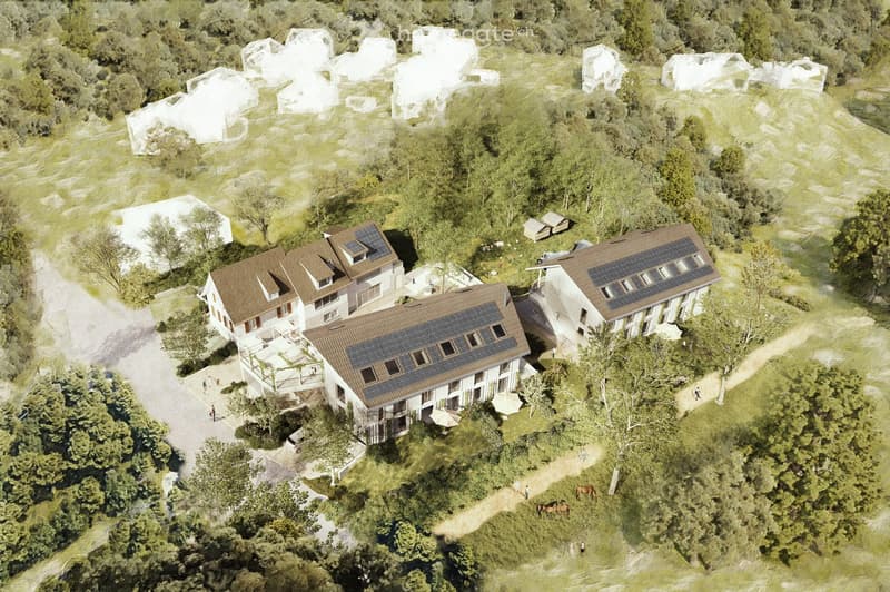 Aerial view of a residential complex with multiple buildings, solar panels on roofs, surrounded by greenery and pathways.