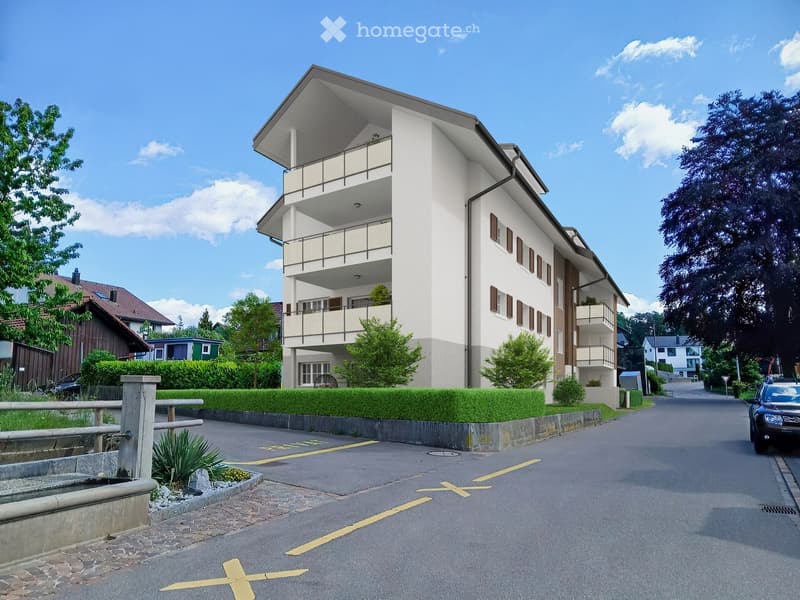 Modern two-story apartment building with white exterior, balconies, and surrounding greenery.