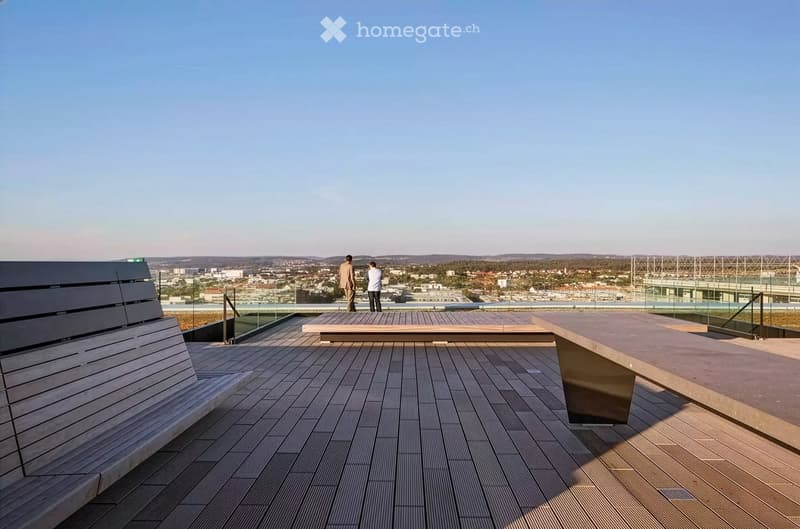 A modern rooftop terrace with wooden decking, glass railings, and a panoramic city view.