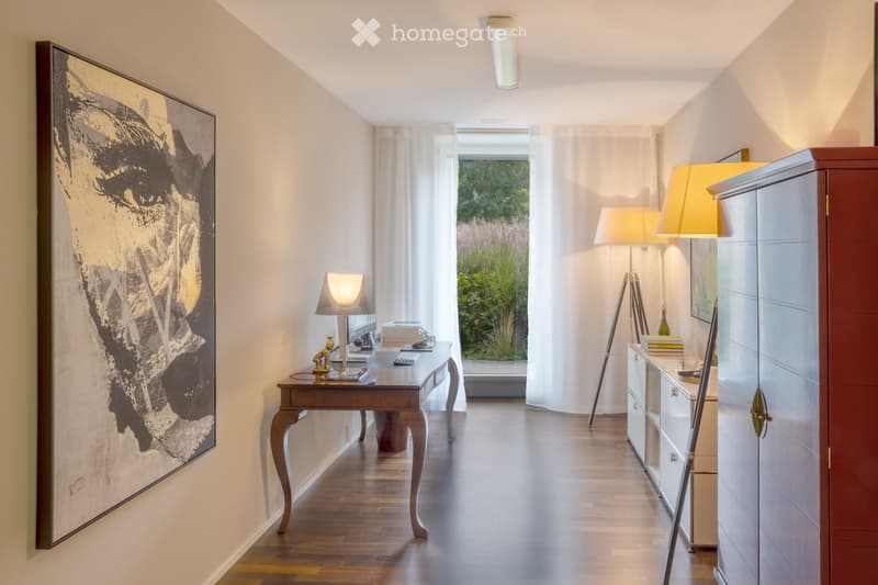 Elegant hallway with wooden flooring, large artwork, a small table with a lamp, and a cabinet with books and decorative items.