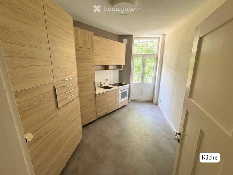 Modern kitchen with light wooden cabinets, a sink, and an oven. The space is bright with large windows and a clean, minimalist design.