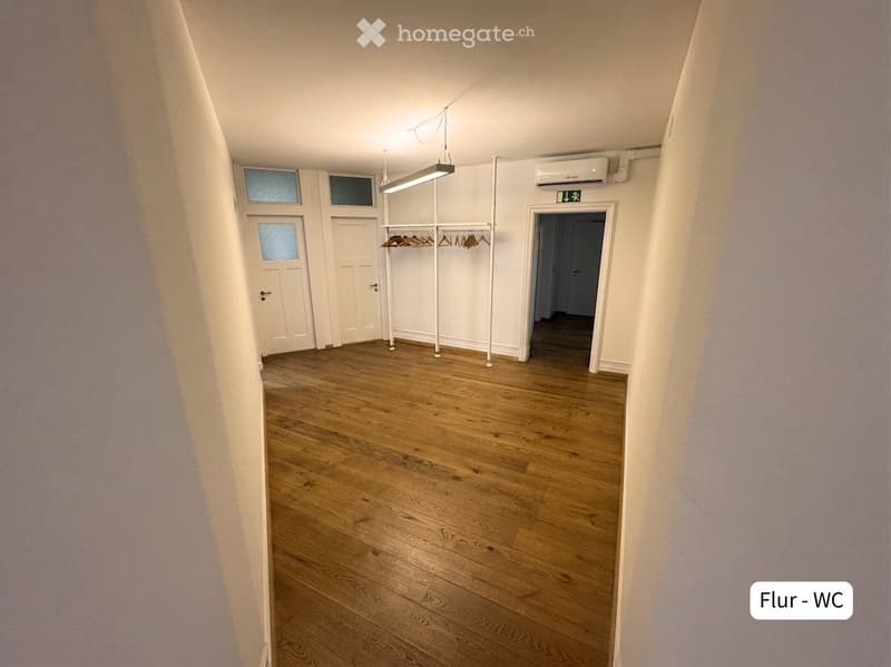Empty hallway with wooden flooring, white walls, and a coat rack with hangers. Doors lead to other rooms.