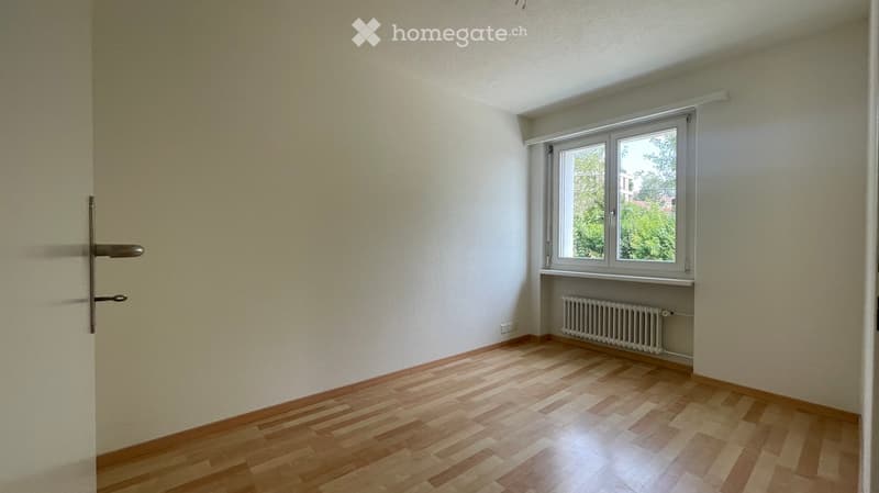 Empty room with wooden flooring, white walls, a window with white frame, and a radiator below the window. No furniture or personal items present.
