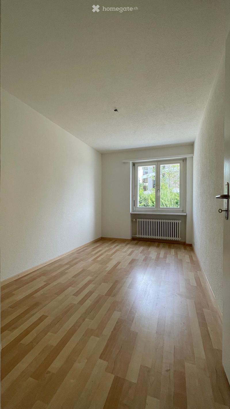 Empty room with wooden flooring, white walls, and a window with a radiator below it.