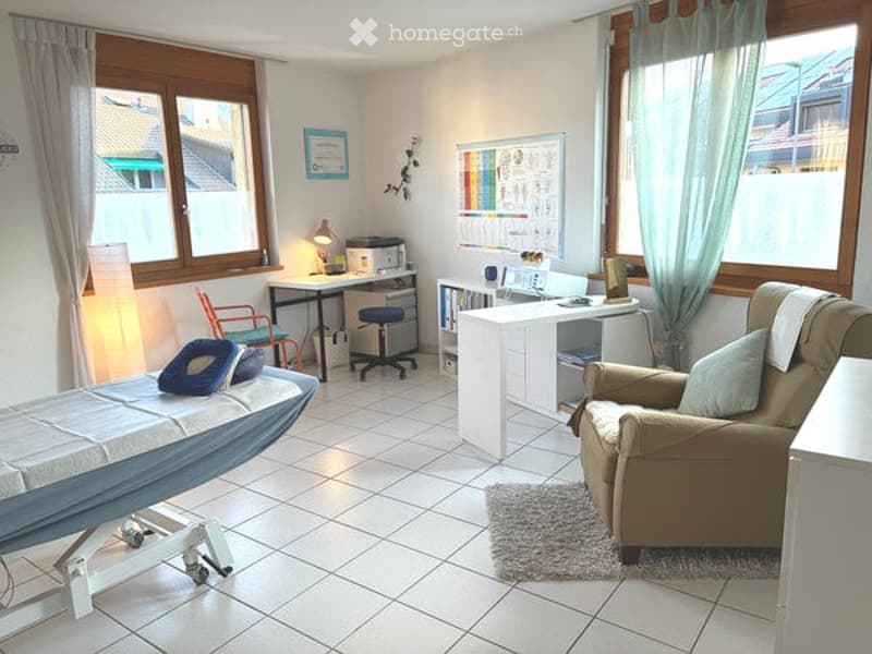 Well-lit room with large windows, a sofa, a small table, a cabinet, a lamp, and a screen. The space appears to be a living or study area with a cozy and organized setup.