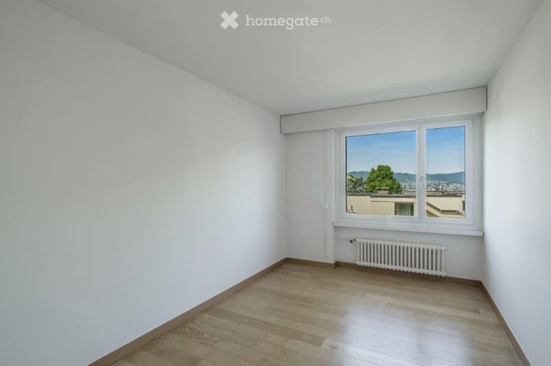 This is an empty room with wooden floors, white walls, and a large window.