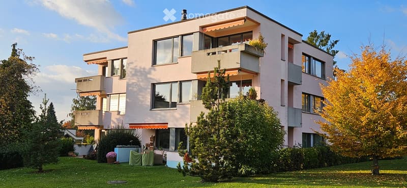 3 story apartment building, pink exterior, multiple balconies, large windows, garden, trees