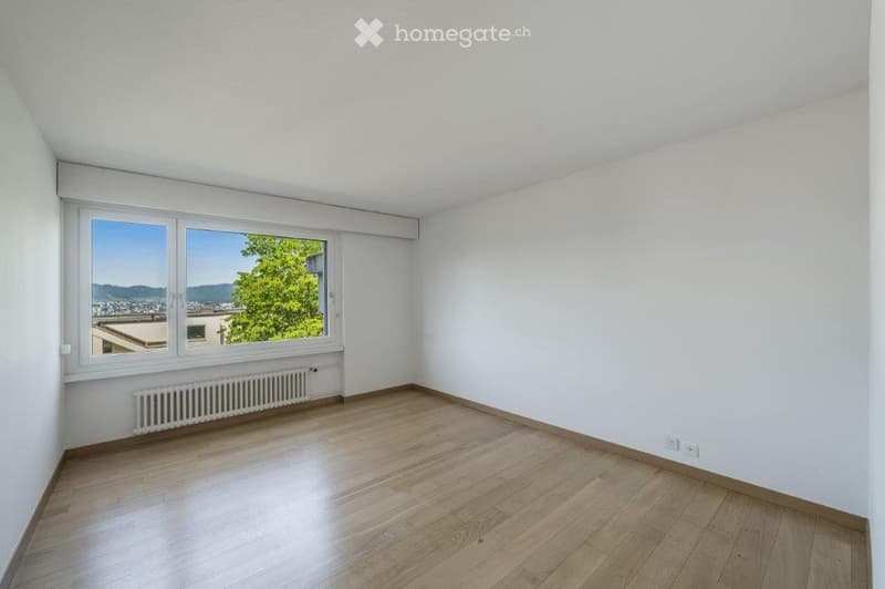 Empty room, white walls, wooden floor, large window with view, white radiator, power outlets