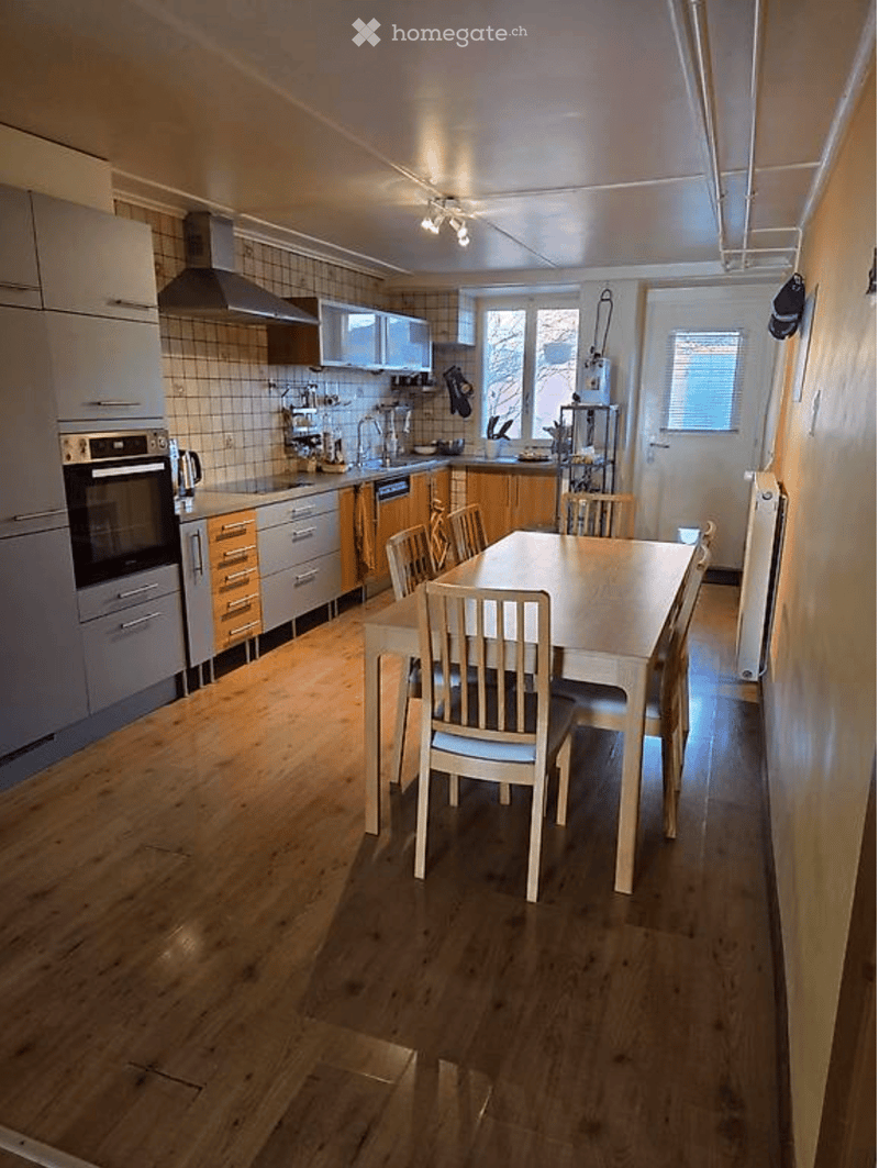 Modern kitchen with light wood flooring, white cabinets, stainless steel appliances, and a dining area with a table and chairs.