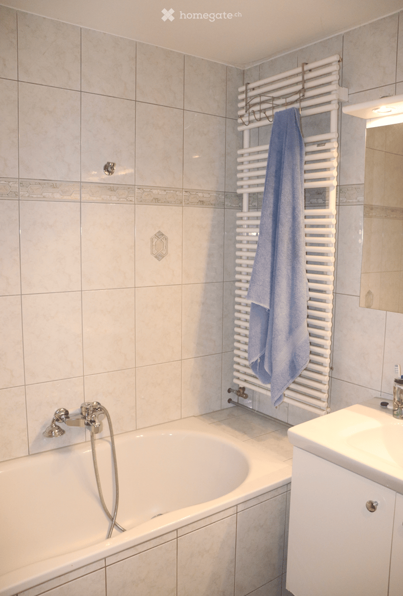 Bathroom with a bathtub, sink, radiator, and a towel hanging on it.