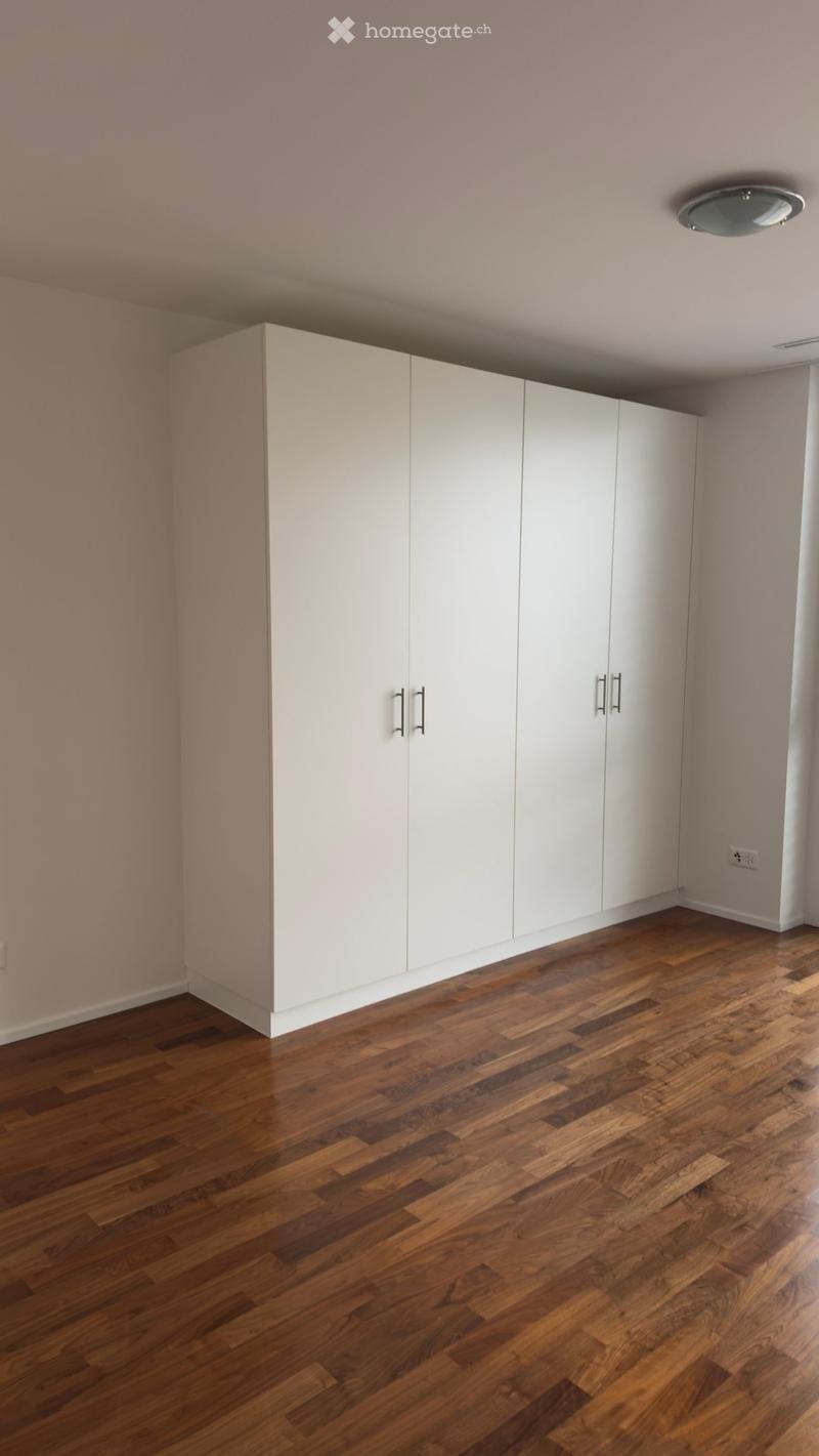 Empty room with light wooden flooring and white built-in wardrobes along one wall.