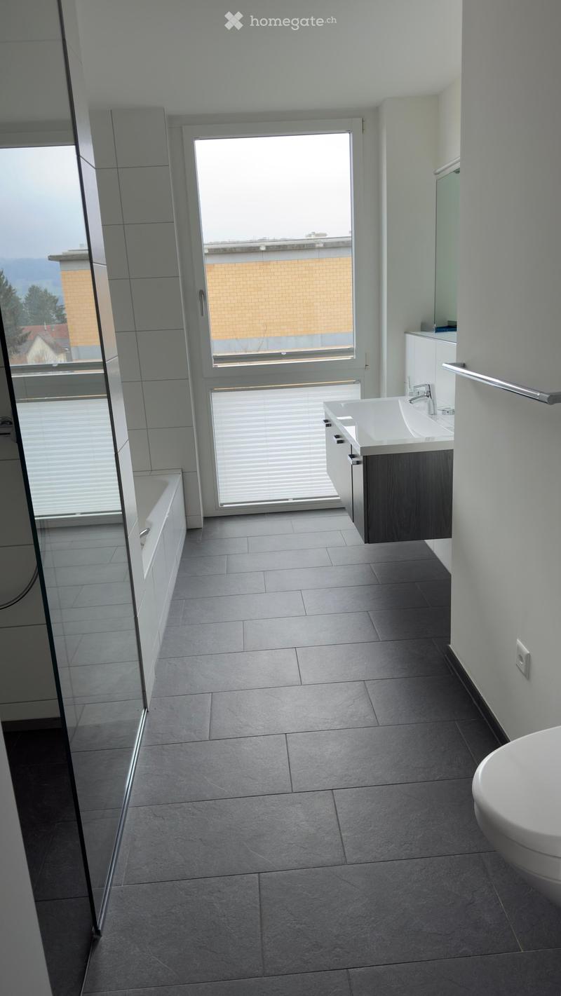 Modern bathroom with a bathtub, sink, toilet, and cabinet. Large window offers a view of the outside.