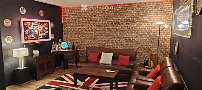 A stylish living room with exposed brick walls, leather sofa, armchair, coffee table, TV, and decorative items on a side table.