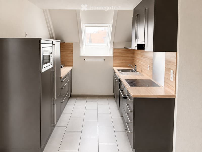 Modern kitchen with dark grey cabinets, light wooden countertops, stainless steel appliances, and a window above the sink.