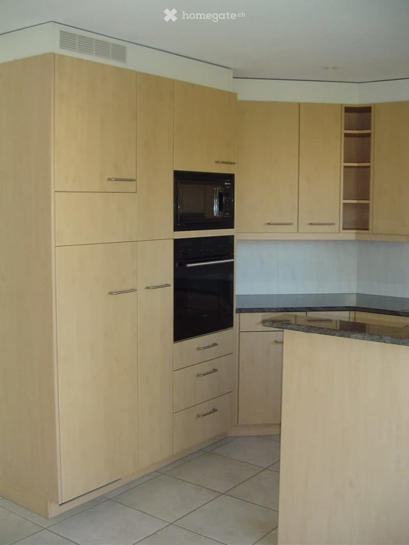 Modern kitchen with light wood cabinets, stainless steel appliances, and a granite countertop.