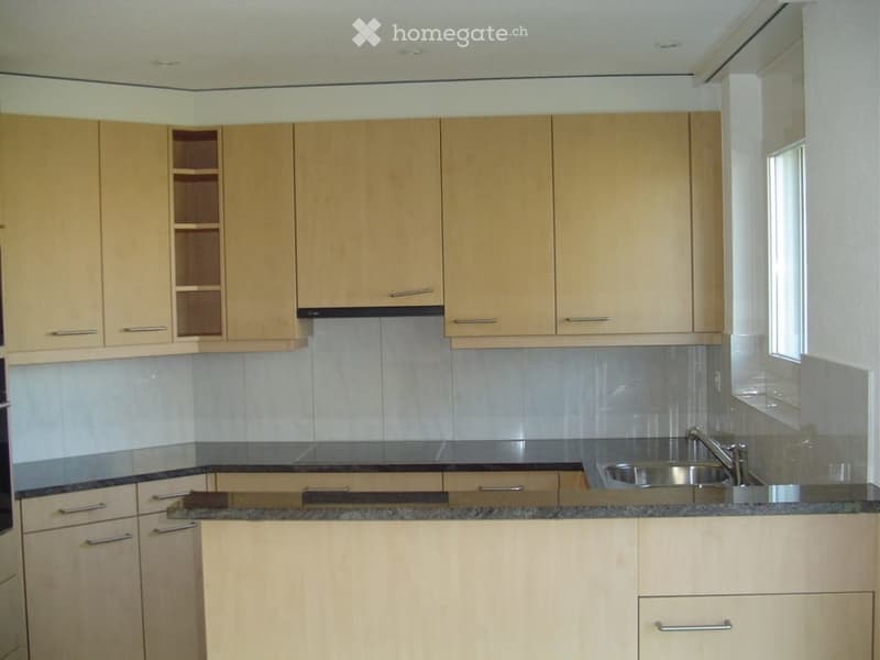 Modern kitchen with light wood cabinets, stainless steel sink, and granite countertop.
