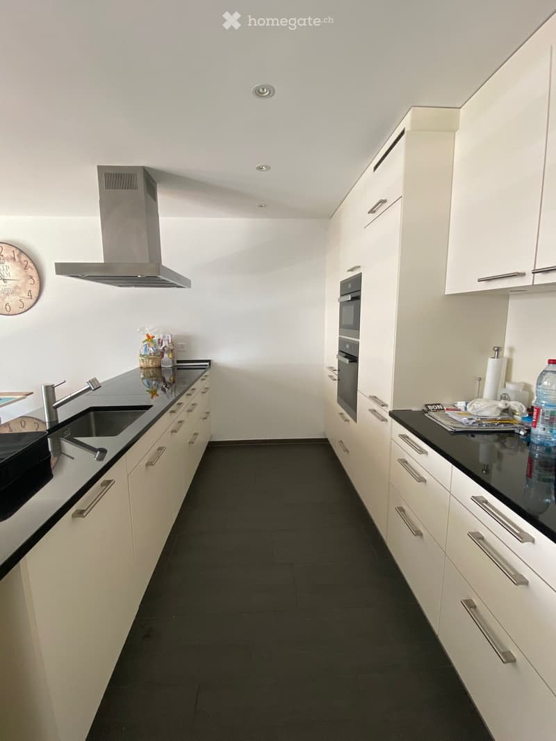 Modern kitchen with white cabinets, black countertops, stainless steel sink, and built-in oven. Features a sleek design with a dark tiled floor.