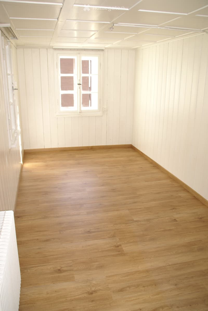 Empty room with wooden flooring, white paneled walls, and a single window with frosted glass panels.