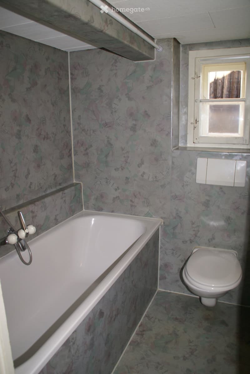 Small bathroom with floral patterned wallpaper, a white bathtub, a toilet, and a window with frosted glass.